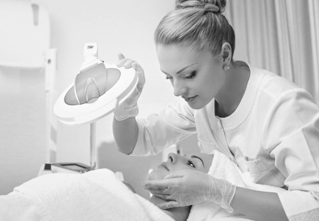 Skincare professional performing a facial treatment using a magnifying lamp on a client in a clinical spa setting