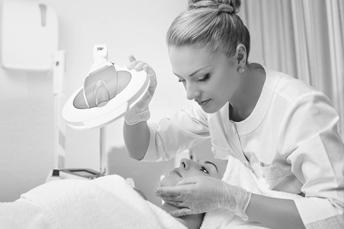 Skincare professional performing a facial treatment using a magnifying lamp on a client in a clinical spa setting