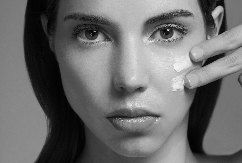 Black and white image of womens face applying skincare cream