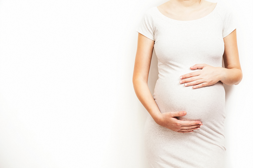 pregnant woman in a white dress holding tummy