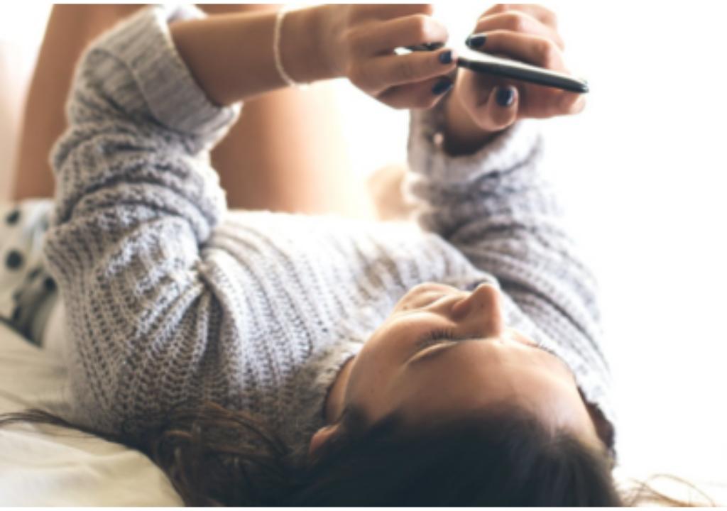 Woman lying on her back while holding a smartphone